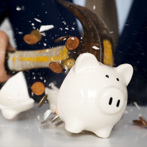 Close-up of businessman using a hammer to smash plenty of coins inside piggybank into pieces as he needs emergency money - using money in financial crisis concept