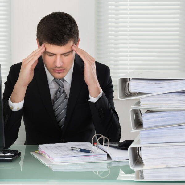 Businessman Suffering From Headache With Invoice On Desk