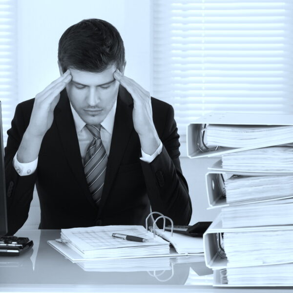 Businessman Suffering From Headache With Invoice On Desk